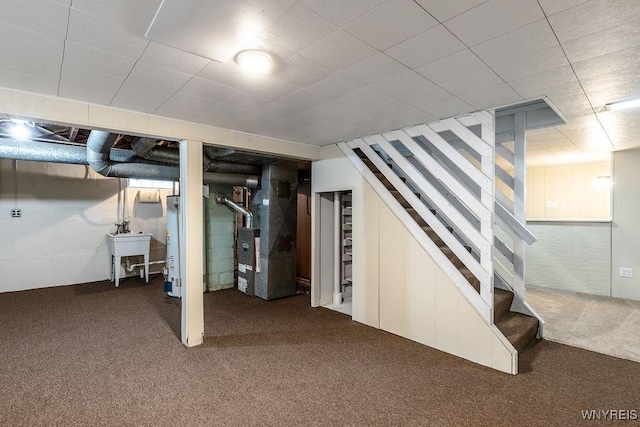 finished basement with heating unit, stairs, carpet floors, water heater, and a sink