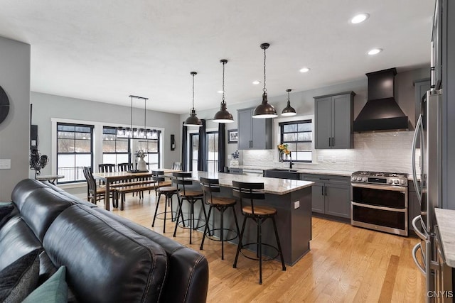 kitchen featuring gray cabinetry, appliances with stainless steel finishes, open floor plan, premium range hood, and a kitchen bar