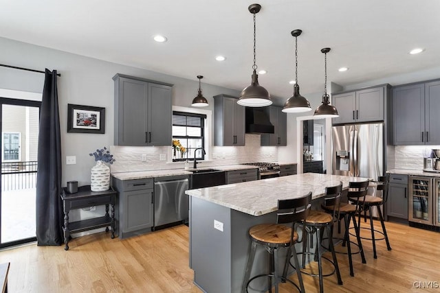 kitchen with beverage cooler, gray cabinets, stainless steel appliances, wall chimney range hood, and a sink