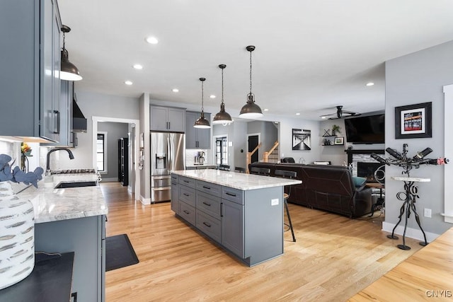 kitchen with gray cabinets, a sink, stainless steel refrigerator with ice dispenser, and light stone countertops