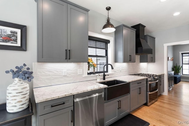 kitchen featuring stainless steel appliances, custom range hood, decorative backsplash, a sink, and light wood-type flooring