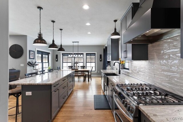 kitchen featuring light stone counters, a kitchen bar, light wood-style flooring, stainless steel gas range oven, and wall chimney exhaust hood