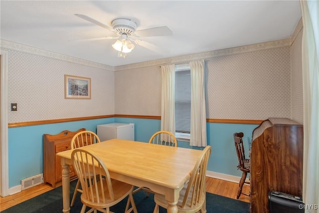 dining room with wood finished floors, wainscoting, visible vents, and wallpapered walls