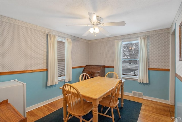 dining area featuring wood finished floors, visible vents, baseboards, and wallpapered walls