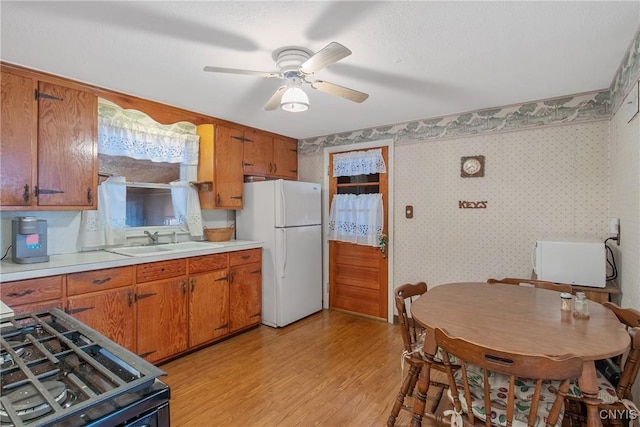 kitchen featuring range with gas stovetop, a sink, freestanding refrigerator, and wallpapered walls