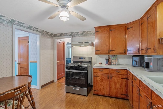 kitchen featuring stainless steel range with gas cooktop, brown cabinets, under cabinet range hood, and wallpapered walls