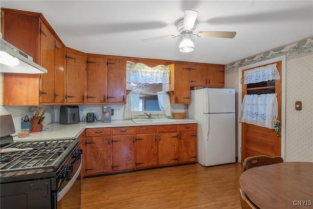 kitchen with a sink, light countertops, freestanding refrigerator, stainless steel range with gas stovetop, and wallpapered walls