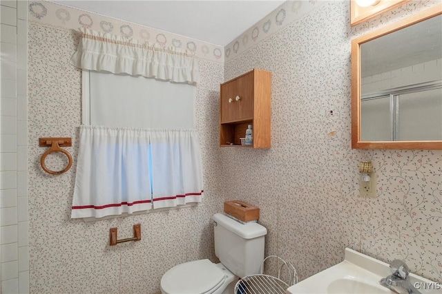 full bathroom featuring a shower with shower door, a sink, toilet, and wallpapered walls