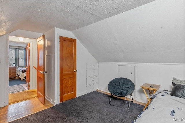 bedroom with vaulted ceiling, a textured ceiling, and wood finished floors