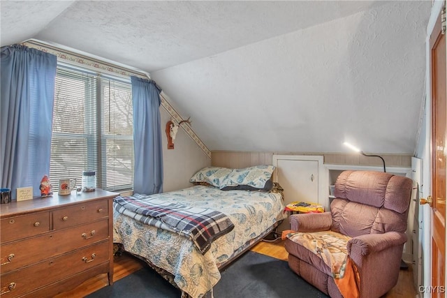 bedroom with lofted ceiling, a textured ceiling, and wood finished floors