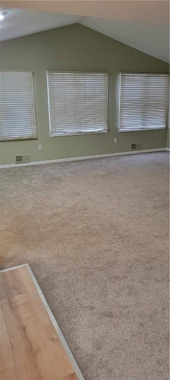 unfurnished room with vaulted ceiling, carpet floors, visible vents, and baseboards