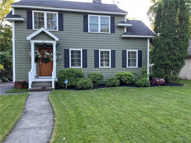 view of front of house featuring a front lawn, a chimney, and a shingled roof