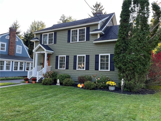 view of front facade featuring a shingled roof, a chimney, and a front lawn