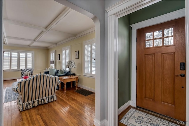 foyer entrance featuring arched walkways, coffered ceiling, visible vents, baseboards, and wood-type flooring