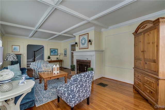 living room featuring arched walkways, coffered ceiling, visible vents, light wood-style floors, and stairs