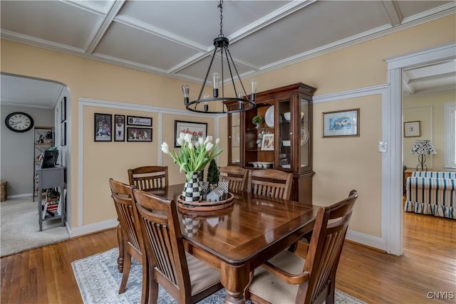 dining area with arched walkways, ornamental molding, wood finished floors, coffered ceiling, and baseboards