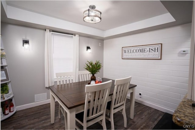 dining area with a tray ceiling, visible vents, dark wood finished floors, and baseboards