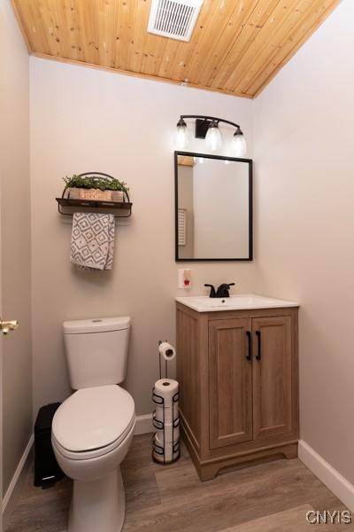 half bath featuring visible vents, toilet, wooden ceiling, wood finished floors, and vanity