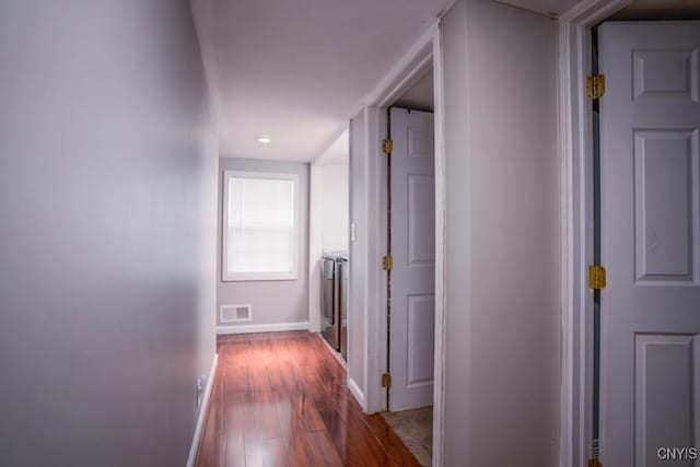 corridor with washer / dryer, baseboards, visible vents, and dark wood finished floors