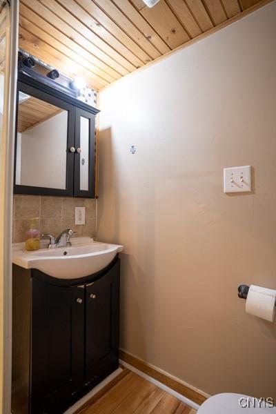 half bath with wooden ceiling, wood finished floors, vanity, baseboards, and tasteful backsplash