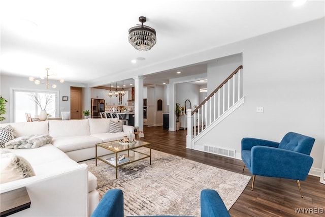 living room featuring a chandelier, visible vents, stairway, and wood finished floors