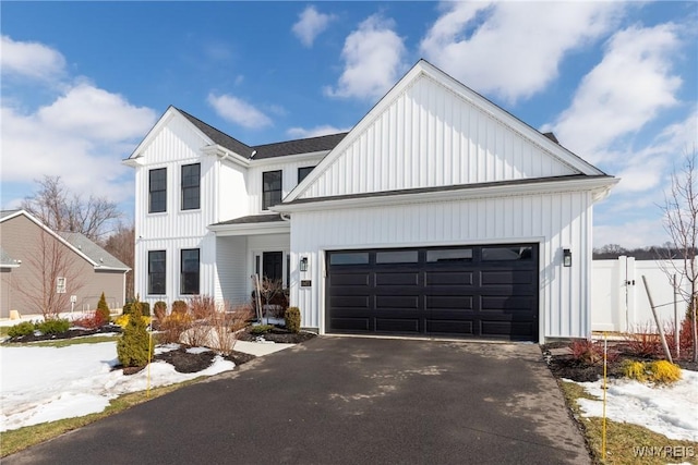 modern farmhouse featuring an attached garage, driveway, fence, and board and batten siding