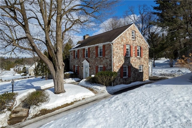 view of snow covered exterior featuring stone siding and a chimney