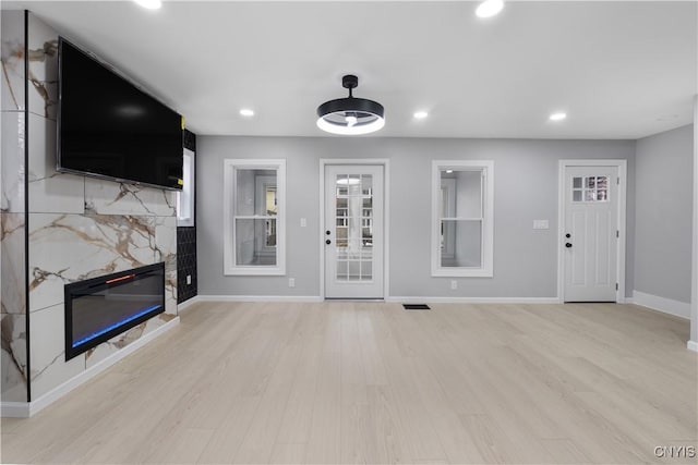 unfurnished living room featuring a glass covered fireplace, baseboards, light wood finished floors, and recessed lighting