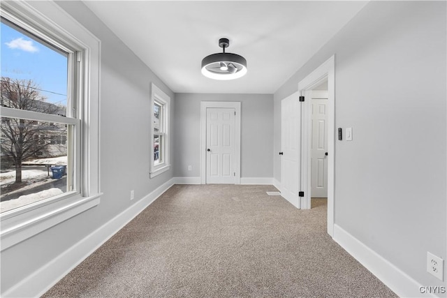 interior space with a ceiling fan, light carpet, and baseboards