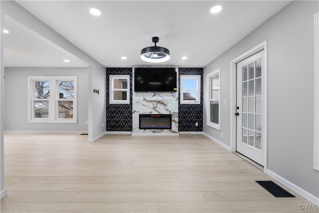 unfurnished living room featuring a high end fireplace, visible vents, light wood finished floors, and recessed lighting