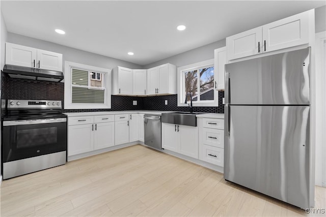 kitchen with appliances with stainless steel finishes, light wood-style floors, white cabinetry, a sink, and under cabinet range hood