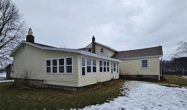 snow covered rear of property with a shingled roof and a chimney