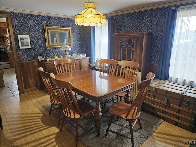 dining room featuring wainscoting, crown molding, light wood finished floors, and wallpapered walls