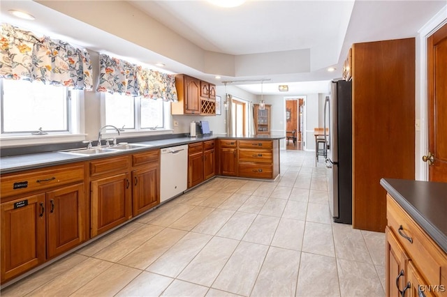 kitchen with brown cabinets, freestanding refrigerator, a peninsula, white dishwasher, and a sink