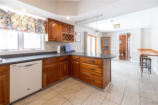 kitchen featuring dark countertops, plenty of natural light, white dishwasher, and brown cabinetry