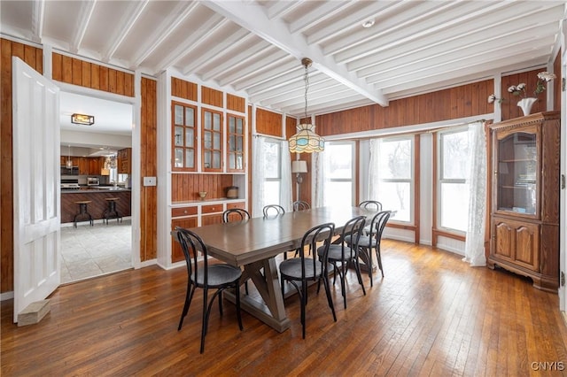 dining space featuring wood walls, beam ceiling, and dark wood-style flooring