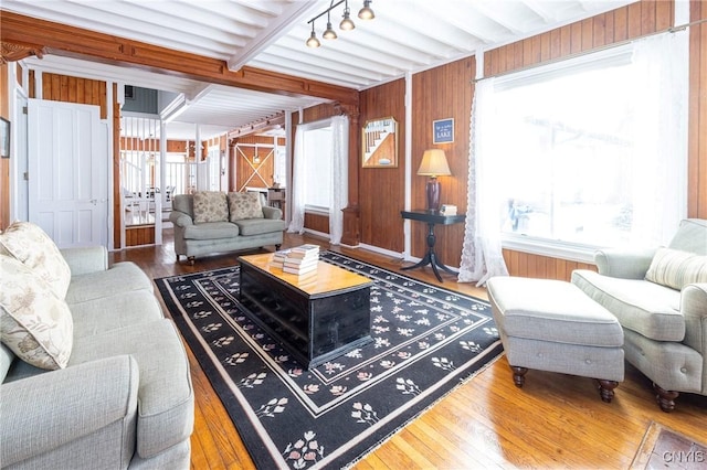 living room with rail lighting, beamed ceiling, wooden walls, and wood finished floors