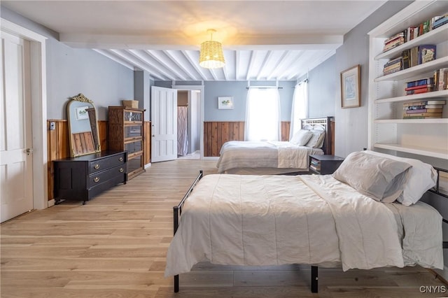 bedroom with light wood-style floors, wood walls, beam ceiling, and wainscoting