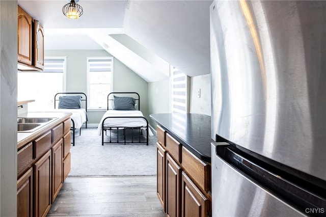 kitchen with lofted ceiling, wood finished floors, a sink, freestanding refrigerator, and dark countertops