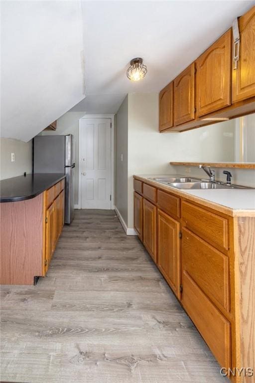 kitchen featuring light wood finished floors, lofted ceiling, brown cabinets, freestanding refrigerator, and a sink