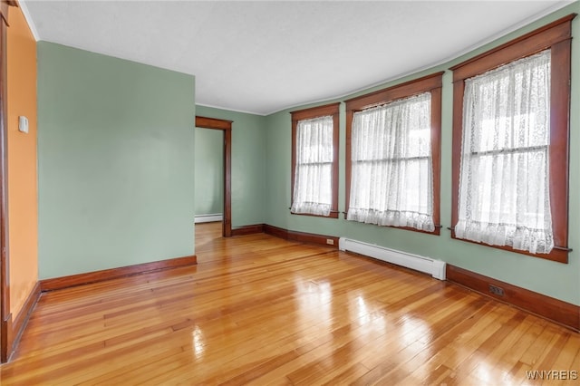 empty room featuring light wood-type flooring, baseboards, and baseboard heating