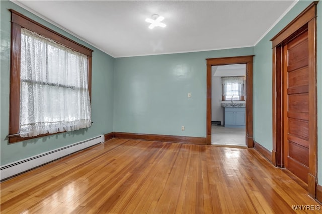 unfurnished room with crown molding, wood-type flooring, a baseboard heating unit, a sink, and baseboards