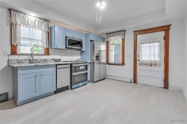 kitchen featuring a baseboard radiator, light stone countertops, stainless steel appliances, blue cabinetry, and a sink