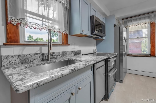 kitchen with appliances with stainless steel finishes, a baseboard heating unit, a sink, and light stone countertops