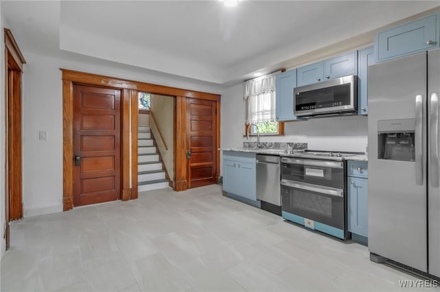 kitchen featuring appliances with stainless steel finishes, a raised ceiling, a sink, and blue cabinetry