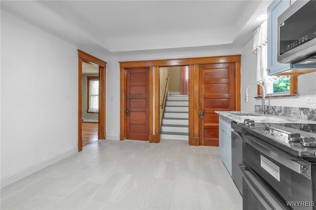 kitchen with range with two ovens, light stone counters, a baseboard radiator, stainless steel microwave, and baseboards