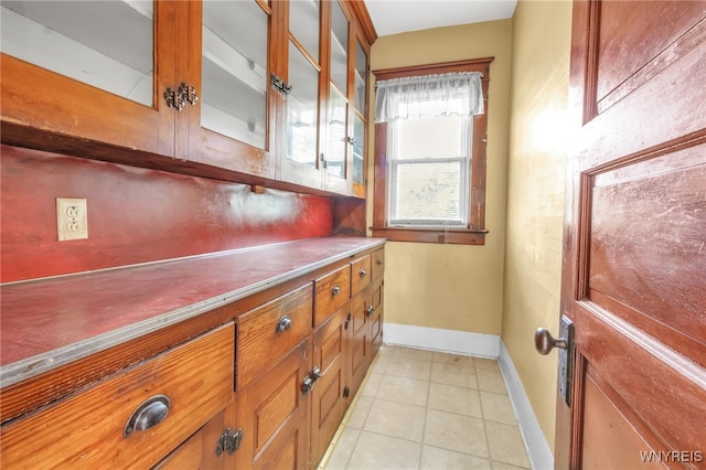 interior space featuring glass insert cabinets, light tile patterned floors, baseboards, and brown cabinets