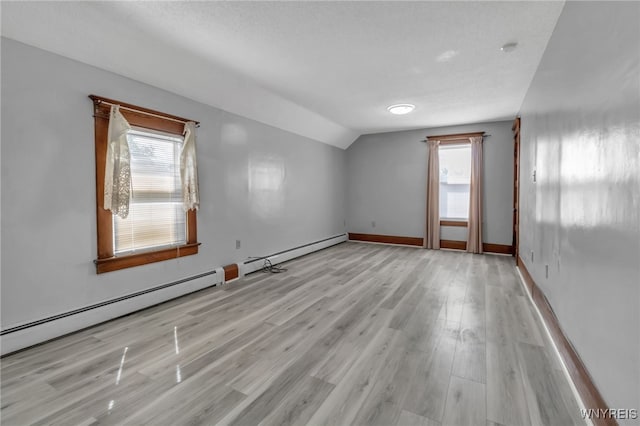 spare room with lofted ceiling, a baseboard heating unit, wood finished floors, and a healthy amount of sunlight