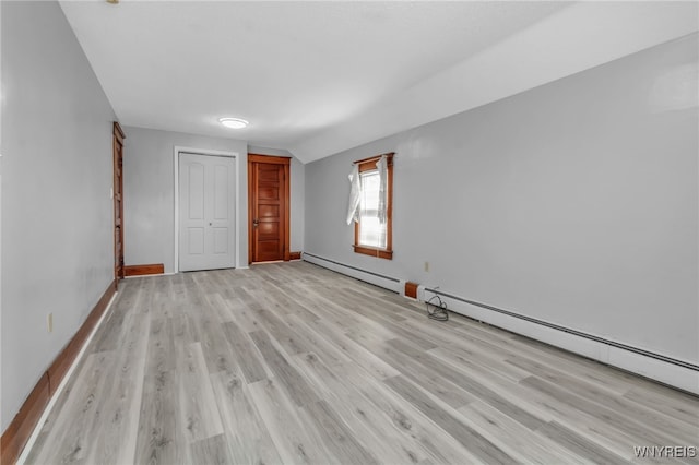 unfurnished bedroom with light wood-style flooring, a baseboard heating unit, baseboards, vaulted ceiling, and a closet