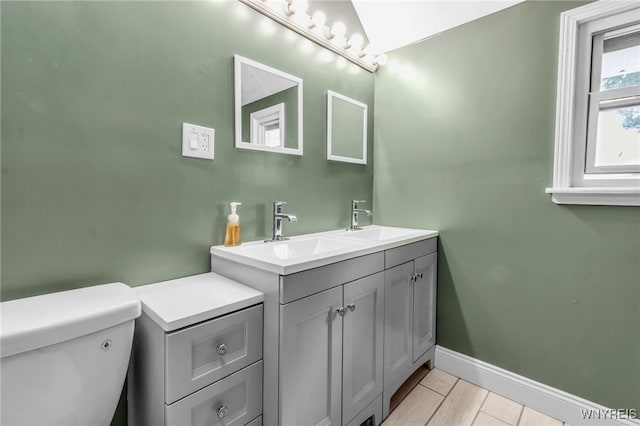 full bath featuring baseboards, a sink, toilet, and double vanity